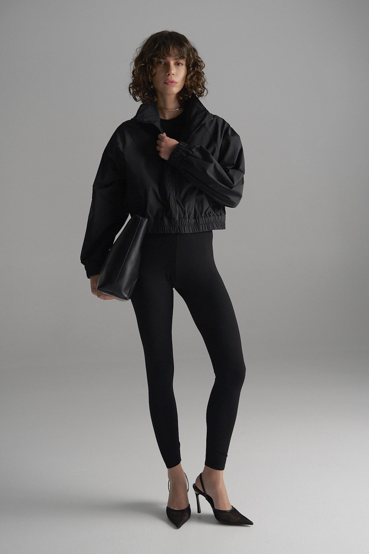 Woman wearing the Mela Purdie Crop Rain Shell in black, styled over tailored trousers. The perfect transeasonal capsule rain jacket. Water repellent women's jacket.